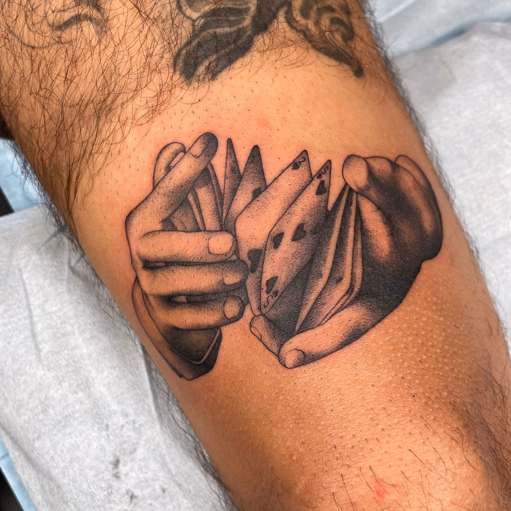 Black and grey tattoo of two hands playing rock, paper, scissors.