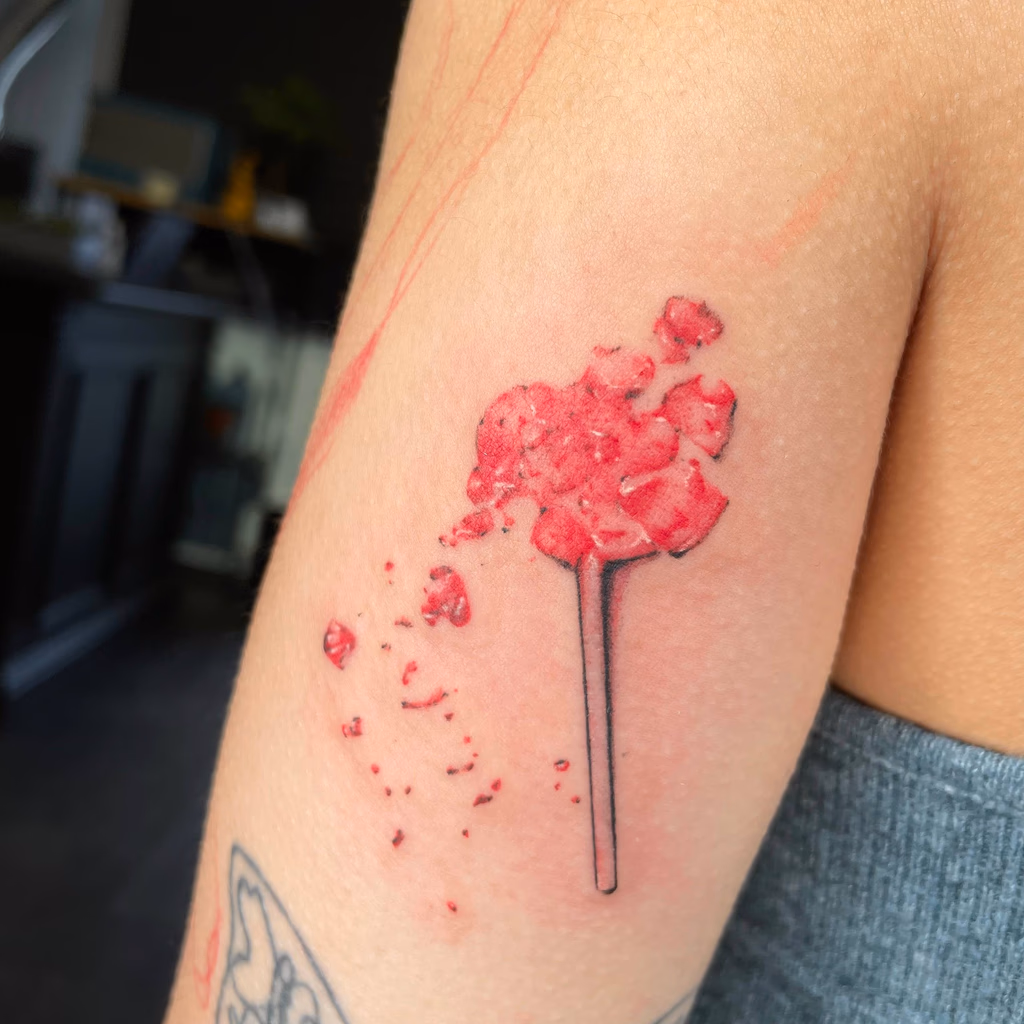 Small red lollipop tattoo with a shattered candy effect.