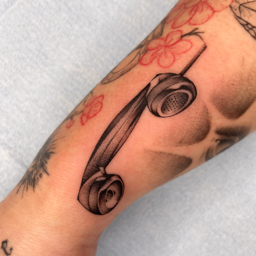 Fine black and grey tattoo of a vintage telephone receiver on an arm.